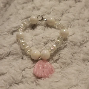 Armband med rosa snäckberlock - Charmigt armband med vita och genomskinliga pärlor samt en rosa snäckformad berlock. Perfekt för att ge en somrig touch till din stil.