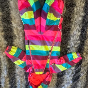 overall från Molo - Säljer en superfin och färgglad overall från Molo i storlek 74. Den har ett coolt randigt mönster i rosa, blått, gult och brunt. Overallen har långa ärmar och dragkedja framtill för enkel påklädning. Perfekt för att lysa upp gråa dagar!