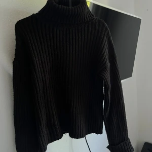 Svart ribbad polotröja från NA-KD - Säljer en supermysig svart ribbad polotröja från NA-KD. Perfekt för kyliga dagar med sin höga krage och långa ärmar. Tröjan är i storlek XS men är oversize. Tröjan är i använt skick 