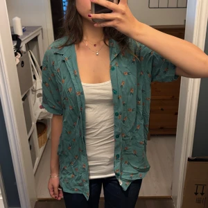 Grön kortärmad skjorta med mönster - Säljer en grön kortärmad skjorta med ett coolt mönster av ananaser. Skjortan är perfekt för sommaren och har en avslappnad passform. Den är i bra skick och redo för nya äventyr! 🌿