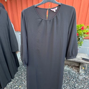 Svart klänning från Indiska - Säljer en elegant svart klänning från Indiska i storlek M. Klänningen har trekvartsärmar och en knytning i midjan för en fin passform. Perfekt för både vardag och fest!