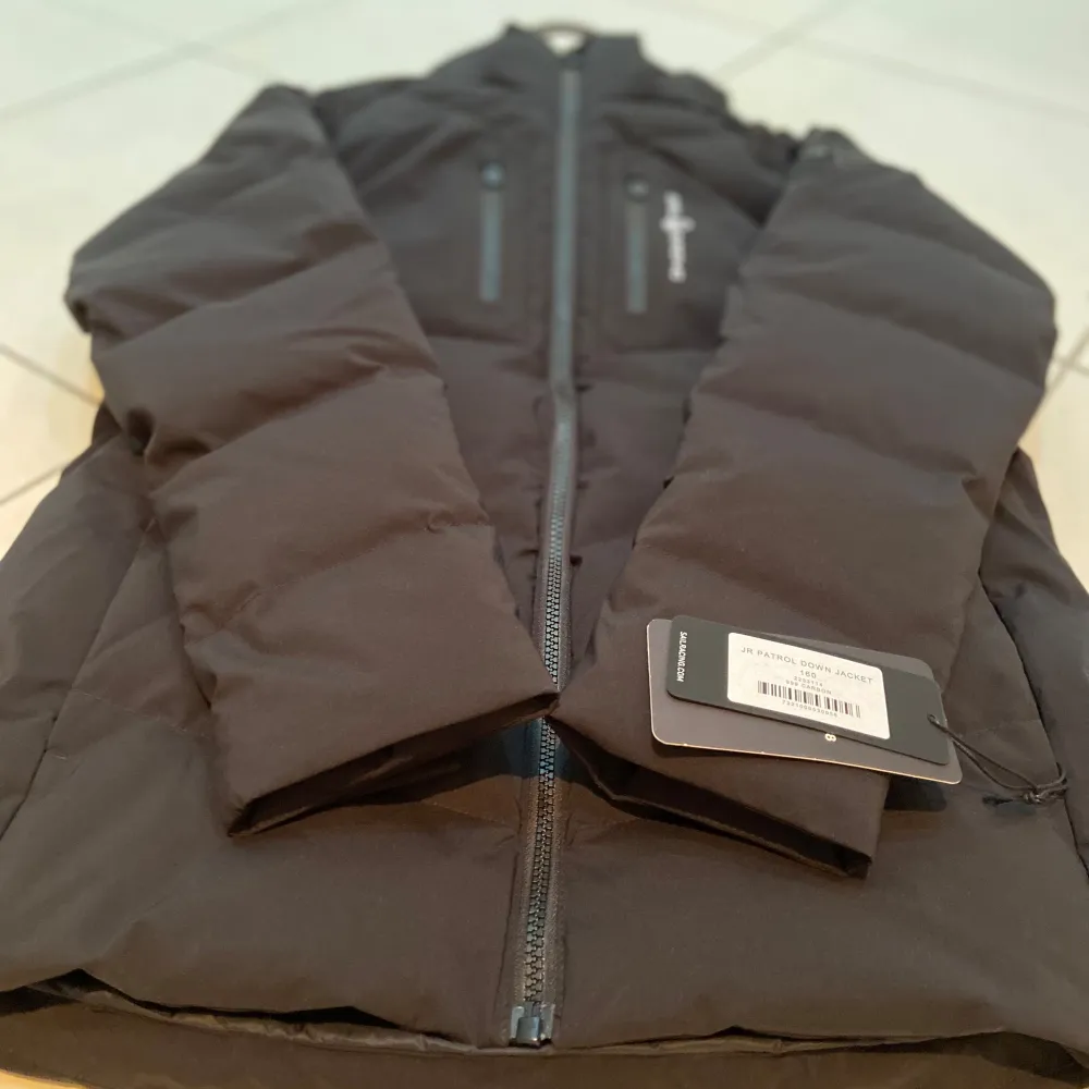 Håll värmen med stil i Svart JR Patrol Down Jacket, storlek 160! Perfekt för killar 13–14 år, med högkvalitativ dunisolering som ger värme utan att kännas tung. Vatten- och vindavvisande med justerbar huva, ribbade ärmslut och praktiska fickor. . Jackor.