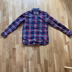 Rutig skjorta från Berkeley - Säljer en snygg rutig skjorta från Berkeley i rött, blått och vitt. Skjortan har långa ärmar och knappar hela vägen ner. Perfekt för en avslappnad stil, men funkar också till festligare tillfällen. Materialet känns skönt och passar bra till både jeans och chinos.