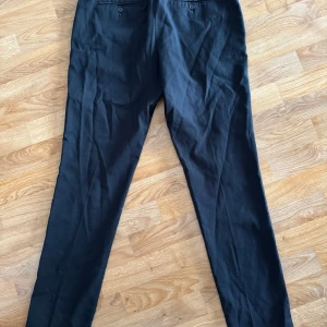 Svarta kostymbyxor - Snygga svarta kostymbyxor med en klassisk design. Byxorna har en rak passform och är perfekta för en stilren look. De har knappar bak och en diskret dragkedja framtill. Mindre i storlek, känns mer som M/L