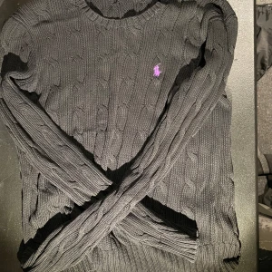 Svart stickad tröja från Ralph Lauren - Säljer en stilren svart stickad tröja från Ralph Lauren med kabelstickat mönster. Tröjan har en lila broderad logo på bröstet. Storleken är M och passar perfa för en grisch o avslappnad look 👀🍾🍾