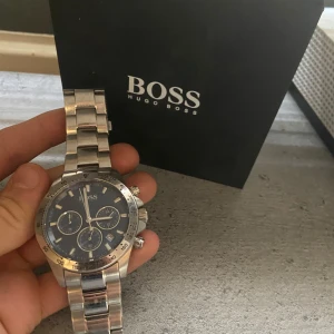 Silverfärgad klocka från Hugo Boss - Snygg och stilren klocka från Hugo Boss i silverfärg med blå urtavla. Klockan har tre mindre urtavlor och en robust länkarmband. Perfekt för den som vill ha en elegant accessoar. Levereras i originalförpackning.