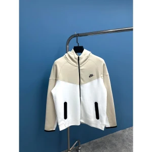 Nike tech beige  - Snygg beige och vit jacka från Nike med dragkedja och huva. Jackan har en stilren design med svarta detaljer och Nike-logga på bröstet. Perfekt för en sportig look. Finns alla storlekar S M L XL XXL