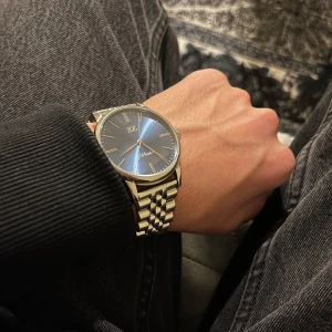 Silverfärgad klocka från KZ - Elegant klocka från KZ med en stilren silverfärgad länkarmband och blå urtavla. Klockan kommer i en snygg förpackning med ett extra svart skinnarmband för variation. Perfekt för den som vill ha en tidlös accessoar.
