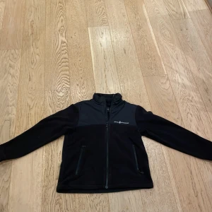 Svart vår jacka från Sail Racing - Säljer en svart fleecejacka från Sail Racing. Jackan har en dragkedja framtill och två praktiska fickor med dragkedjor. Den är långärmad och har en hög krage för extra värme. Perfekt för kyliga dagar! Säljer pga tröttnat men passar perfekt till den som har en klassisk look och vill ha en det jacka till våren