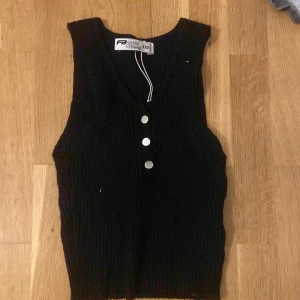 Svart ribbad topp från Sister Knitwear - Snygg svart ribbad topp  från Sister Knitwear med tre knappar framtill. Perfekt för lager-på-lager och ger en stilren look. Passar bra till både jeans och kjol. Tröjan stretchas ut när man tar på sig den. Jätte snygg topp till sommaren💗👾