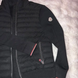 Svart jacka från Moncler - Snygg svart jacka från Moncler med quiltad design och dragkedja. Jackan har långa ärmar och en huva för extra skydd. Perfekt för kyligare dagar med stilren look.