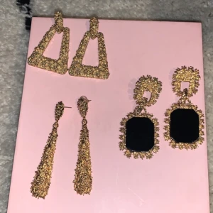 Tre par glittriga örhängen - Säljer tre par glittriga örhängen i guld. Ett par har en triangulär form, ett annat par är långa och smala, och det tredje paret har en rektangulär svart detalj i mitten. Perfekta för att lysa upp vilken outfit som helst! 30kr st