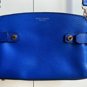 Blå axelväska från Henri Bendel - Snygg blå axelväska från Henri Bendel i skinn med justerbar axelrem och dragkedja. Perfekt för att bära dina nödvändigheter med stil. Väskan har eleganta metallknappar som detaljer.