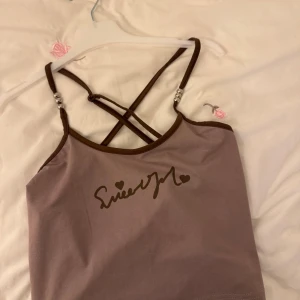 Lila linne med text och pärldetaljer - Säljer ett lila linne med bruna axelband och texten 'Sweet Girl' framtill. Linnet har korsade axelband med silverpärlor som detalj. Perfekt för en avslappnad stil.