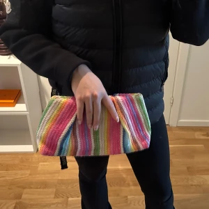 Väsk - Säljer en superfin kuvertväska med färgglada ränder i rosa, grön, gul, blå och orange. Perfekt för att liva upp vilken outfit som helst! Väskan är kompakt och lätt att bära med sig.