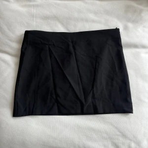 Svart kostym kjol från Gina Tricot - Snygg svart kostym kjol från Gina Tricot. Perfekt för en stilren look. Kjolen har en enkel design och är lätt att matcha med olika toppar.