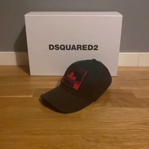 Svart keps från Dsquared2 - Snygg svart keps från Dsquared2 med röd broderad patch framtill och justerbart spänne bak. Perfekt för en cool och avslappnad stil. Denna är en limited edition och kan inte köpas längre