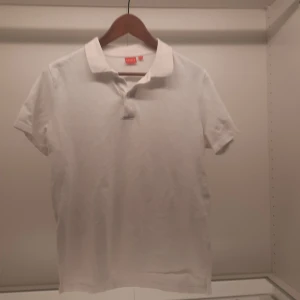 Vit pikétröja från RYVLS - Säljer en stilren vit pikétröja från RYVLS. Tröjan har en klassisk krage och knappar framtill. Perfekt för en avslappnad och snygg look. Passar bra till både jeans och shorts.