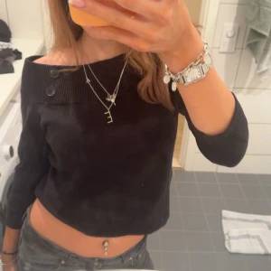 Svart offshoulder tröja med knappar - Säljer en stilren svart offshoulder tröja med dekorativa knappar på axeln. Tröjan har trekvartsärmar och en croppad passform som ger en trendig look. Perfekt för att skapa en chic outfit! Storlek M sitter som S aldrig använd!