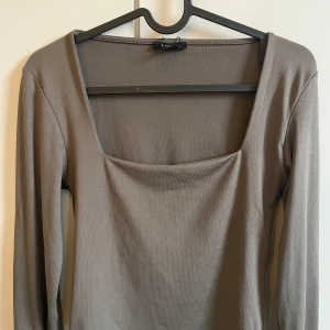 Grå långärmad topp från Aéryne - Snygg grå långärmad topp från Aéryne med en elegant fyrkantig urringning. Perfekt för en stilren look. Passar bra till både jeans och kjol. Enkelt att matcha med olika accessoarer för att skapa din egen stil.