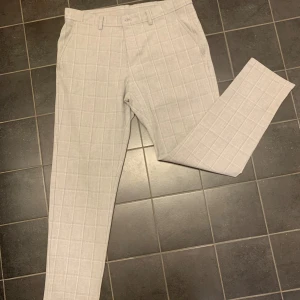 Grå rutig kostymbyxa från Zara - Snygga grå kostymbyxor från Zara med ett diskret rutmönster. Byxorna har en klassisk passform med knappar och dragkedja i midjan. Storlek 42.