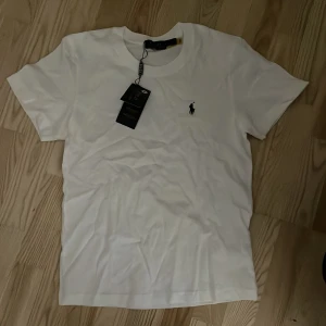 Vit t-shirt från Polo Ralph Lauren - Säljer en klassisk vit t-shirt från Polo Ralph Lauren med det ikoniska broderade logotypen på bröstet. T-shirten är kortärmad och tillverkad i mjuk bomull för en bekväm passform. Perfekt för en stilren look.
