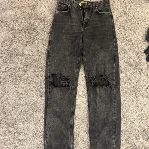 Svarta jeans från Gina Tricot -  svarta jeans från Gina Tricot med slitningar på knäna. De har en klassisk femficksdesign och en knappgylf. 