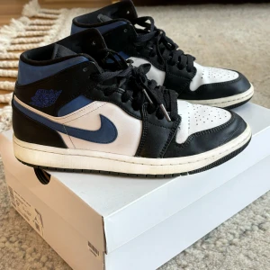 Nike Air Jordan 1 MID  - Snygga Nike Air Jordans i en klassisk färgkombination av svart, vit och blå. Bra skick och köpta för 2000kr på GOAT.