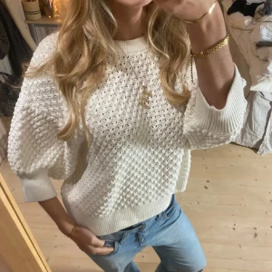 Vit stickad tröja - Säljer en snygg vit stickad tröja med puffiga ärmar och ett fint hålmönster. Tröjan har ribbade muddar vid ärmslut och nederkant, vilket ger en skön passform. Perfekt för en stilren look.