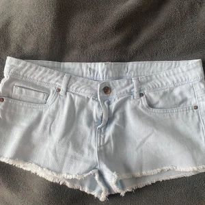 Lågmidjade jeansshorts  - Snygga ljusblå lågmidjade jeansshorts med fransiga kanter. Perfekta för sommardagar och avslappnade stunder. Klassisk femficksdesign med knapp och dragkedja framtill. Kom privat för bilder på 💞