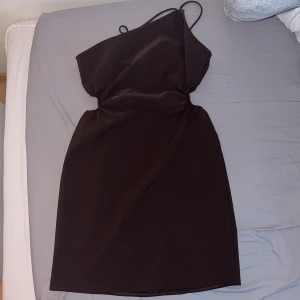 Brun one-shoulder klänning - Riktigt snygg brun one-shoulder klänning i storlek 36/S med en elegant och stilren design från GinaTricot. Klänningen har två hål så midjan syns på sidorna. 