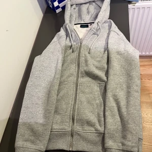  Superdry Hoodie - Säljer en grå hoodie från Superdry med dragkedja och justerbar huva. Tröjan har ribbade muddar och en broderad logga på bröstet. Använd 1 gång förut och i skick 10/10😇 Nypris 1000 kr😇😇😇