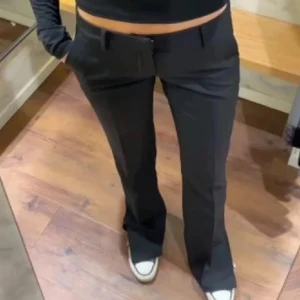 Svarta lowwaist kostymbyxor med bootcut - Snygga populära svarta lowwaist kostymbyxor med en klassisk bootcut-stil. Byxorna har en lågmidjad passform och stängs med dragkedja och knappare. Perfekta för en stilren look.