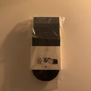 Svarta strumpbyxor från H&M - Säljer ett par svarta strumpbyxor från H&M. De är förpackade i plast och har en enkel design. Perfekta för att komplettera din outfit med en klassisk look.
