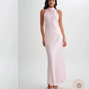 Ljusrosa långklänning från meshki - Elegant ljusrosa långklänning i satin från meshki. Klänningen är ärmlös med en hög hals och öppen rygg, vilket ger en sofistikerad look. Perfekt för speciella tillfällen. Helt oanvänd! Storlek XXS.