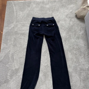 Mörkblå juicy cotore byxor   - Snygga blåa  byxor med fickor bak och knappdetaljer. Perfekta för en avslappnad stil. Materialet ser mjukt och bekvämt ut, vilket gör dem idealiska för vardagsbruk.