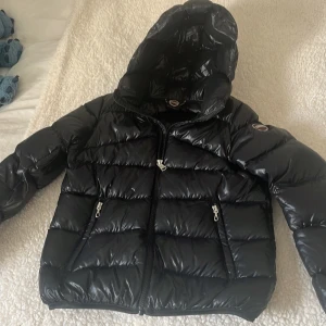 Svart pufferjacka från Colmar - Snygg svart pufferjacka från Colmar med glansig finish och huva. Jackan har dragkedja framtill och två praktiska fickor med dragkedjor. Perfekt för kyliga dagar när du vill hålla stilen. 🖤Kan gå ner i pris