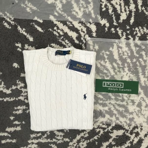 Vit stickad tröja från Polo Ralph Lauren cable knit/ kabel stickad - Säljer en stilren vit stickad tröja från Polo Ralph Lauren med klassiskt kabelstickat mönster. Den är nästan helt ny och har använts en gång efter att jag fick den i julklapp. 