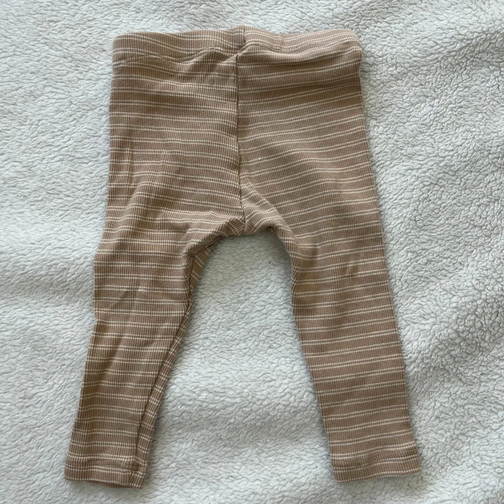 Säljer ett par söta beige och vita randiga leggings för baby från Lindex. De är mjuka och bekväma, perfekta för de minsta. Leggingsen har en liten etikett med en regnbåge på sidan.. Farkut & Housut.