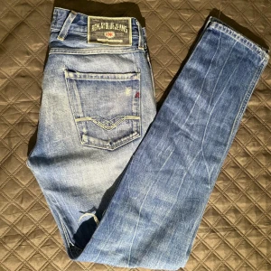 Jeans Replay - Ett par ljusblåa jeans från Replay med passformen slim (Anbass). Storleken är i midja 30 och längd 32. Den har riktigt feta slitningar vid knäna samt en stilig tvätt över hela jeansen. Hör av dig vid funderingar!