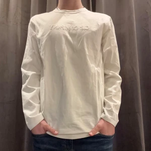 Vit långärmad tröja från C.P. Company - Säljer en stilren vit långärmad tröja från C.P. Company. Tillverkad i 100% merceriserad bomull för en mjuk och lyxig känsla. Perfekt för en avslappnad men ändå snygg look. Tröjan har en diskret logga på bröstet.