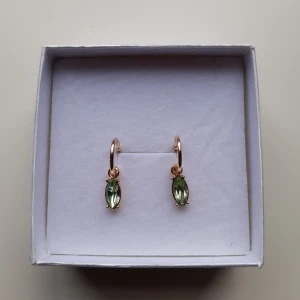 Guldörhängen med gröna stenar - Eleganta guldörhängen med hängande gröna stenar i en droppform. Örhängena har endast använts ett fåtal gånger och är därför i mycket bra skick. De hängande gröna stenarna går även att ta av från örhänget, om man önskar. Skriv gärna vid frågor.