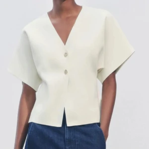 Vit kortärmad blus med knappar - Säljer en stilren vit blus med korta ärmar och v-ringning. Blusen har två dekorativa knappar framtill och en rak passform. Perfekt för en elegant och avslappnad look. Enadast testad så i nyskick!