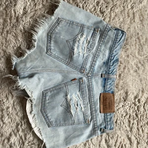 Ljusa jeansshorts med slitningar - Säljer ett par ljusa jeansshorts med coola slitningar och fransiga kanter. Står ingen storlek men skulle gissa på 34🥰