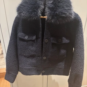 Mörkblå ulljacka med pälsdetaljer - Snygg mörkblå ulljacka med en fluffig pälsdetalj på kragen. Jackan har knappar framtill och två fickor med lock. Perfekt för kyliga dagar när du vill hålla stilen. 🧥✨