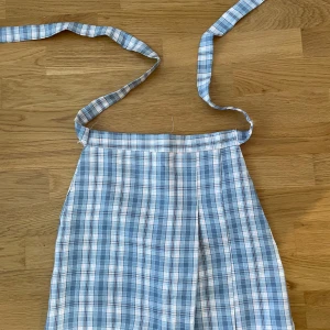 Rutig kjol  - Charmig rutig kjol i blå och rosa toner med ”osynlig” dragkedja baktill (bild 3). OANVÄND.  Kjolen har ett klassiskt rutmönster och ett band i midjan för rosett. Veckad (Två veck).  Tunna fastsydda shorts innanför (bild 4).  Asiatisk storlek S (brukar vara små i storlekarna), köpt från Lianox. 