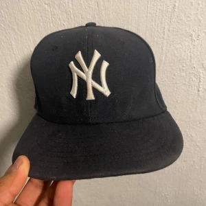 Svart keps från New Era - Snygg svart keps från New Era med broderad vit logga på framsidan. Kepsen har en klassisk design och är perfekt för sportiga tillfällen. Tillverkad i ett slitstarkt material med en bekväm passform. Den är äkta 