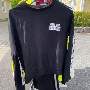 Svart tröja med texten 'Rebel Girl Revolution' - Säljer en svart tröja med texten 'Rebel Girl Revolution' tryckt på bröstet. Tröjan har långa ärmar med text längs sidorna, vilket ger en edgy look. Perfekt för en avslappnad stil eller för att göra ett statement. Passar bra till jeans eller leggings! 