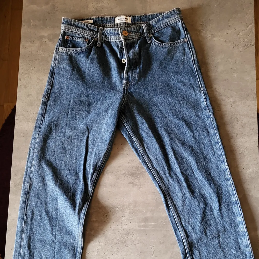 Säljer ett par blå jeans från Jack & Jones i storlek L. De är i loose fit och har en klassisk femficksdesign med knappar och dragkedja. Perfekta för en avslappnad stil!. Jeans & Byxor.