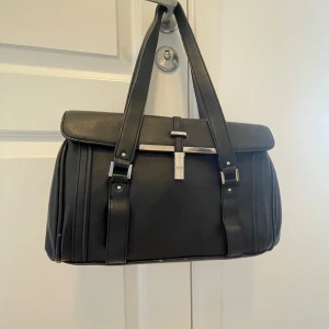 Väska  - Säljer en svart handväska som är medelstor och rymmer hyfsat mkt. Det finns 2 stora innerfack och 2 små + 1 litet på utsidan. Är i fint skick förutom några få skavsår i botten, se bild 3